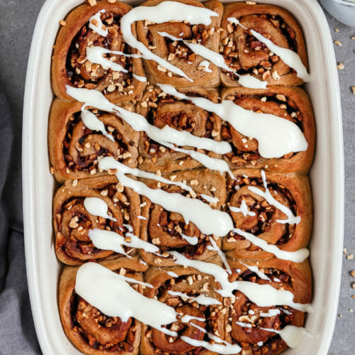 Vegane Zimtschnecken Rollen mit Apfel Zimt Füllung und einem Cream Cheese Frosting. Platziert sind die Zimtschnecken in einer Auflaufform.