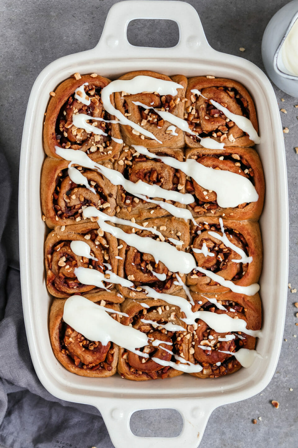 Vegane Zimtschnecken Rollen mit Apfel Zimt Füllung und einem Cream Cheese Frosting. Platziert sind die Zimtschnecken in einer Auflaufform.