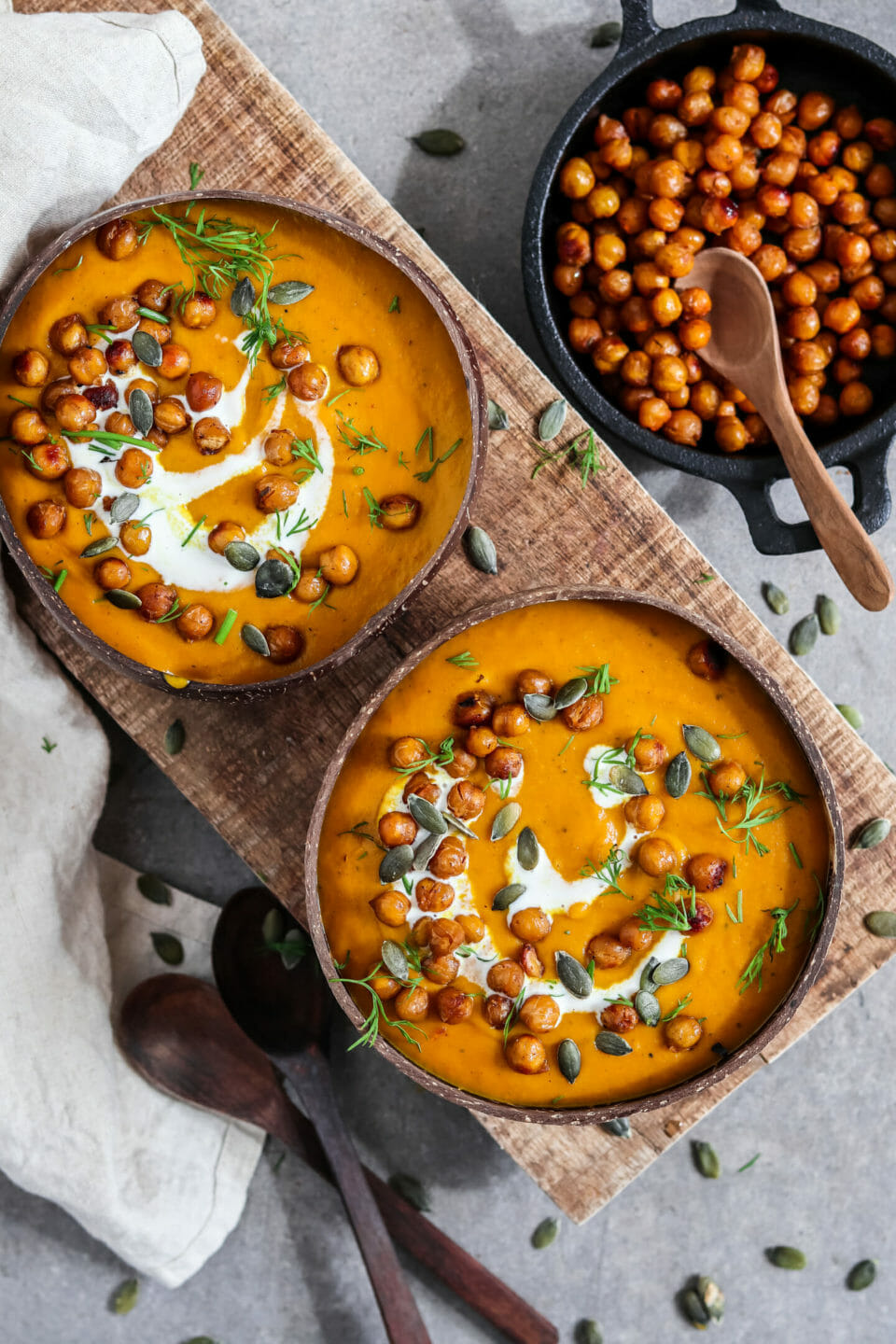 Pürierte Kürbissuppe in zwei Kokosnussschalen serviert mit einem Schuss Kokosnussmilch, Kichererbsen und Kürbiskerne