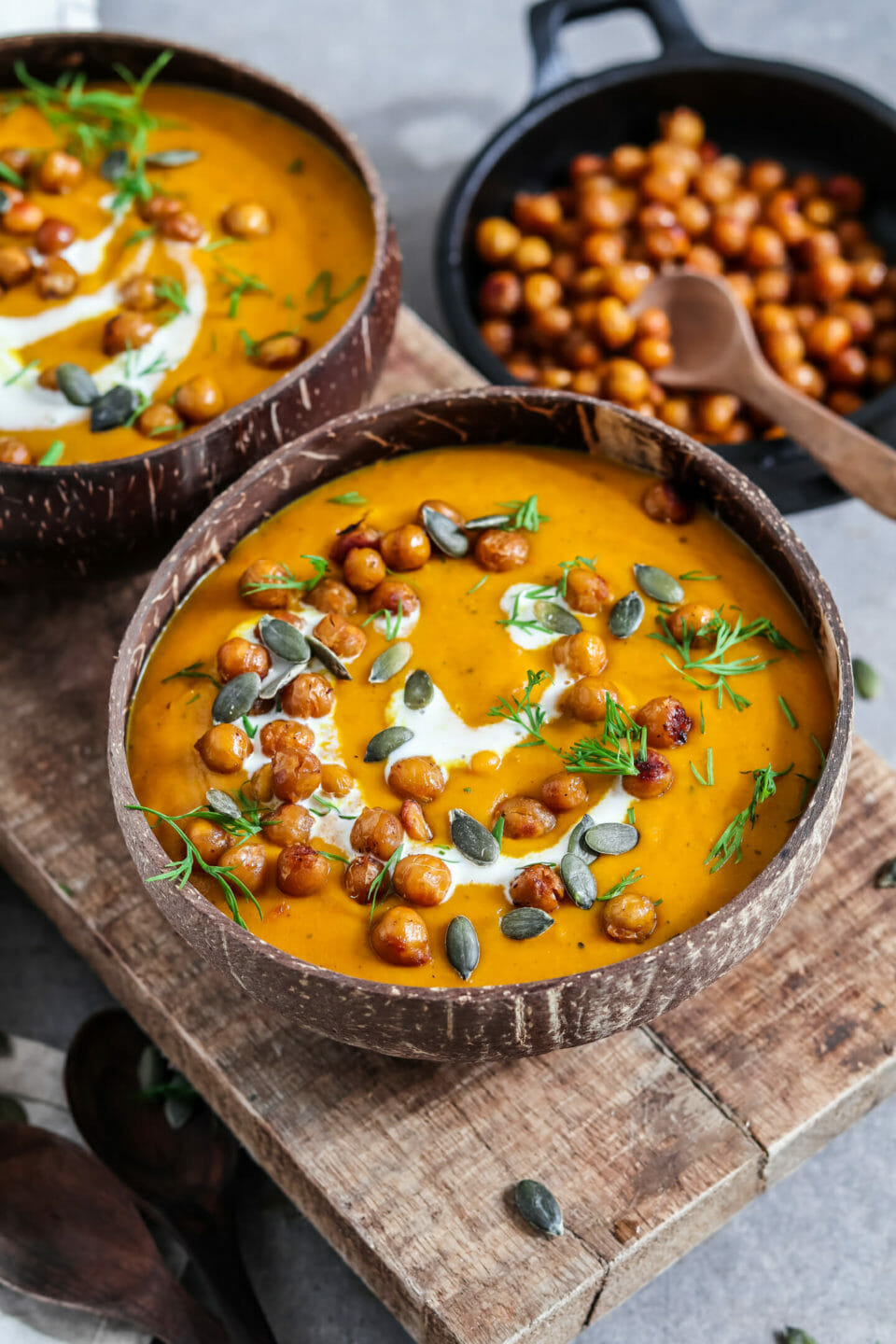 Pürierte Kürbissuppe in zwei Kokosnussschalen serviert mit einem Schuss Kokosnussmilch, Kichererbsen und Kürbiskerne