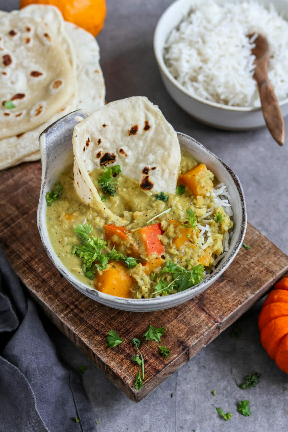 Veganes Linsen Curry mit Kürbis serviert in einer Schale mit Reis und selbst gemachten Fladenbrot.