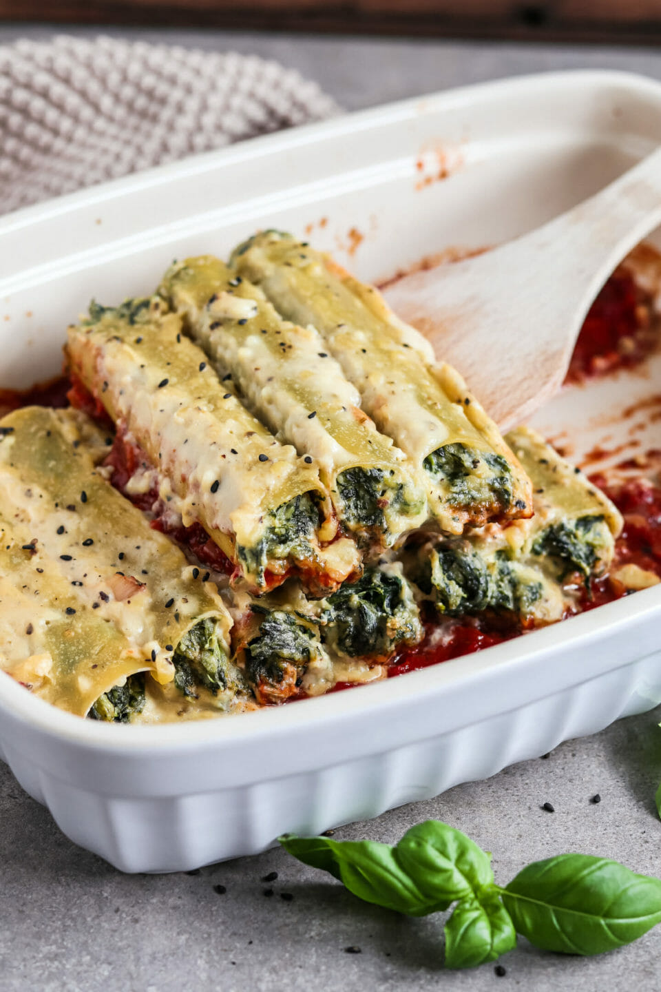 Mit Spinat Ricotta gefüllte Cannelloni aus dem Ofen mit Tomatensauce und Bechamelsauce, serviert in einer Auflaufform.