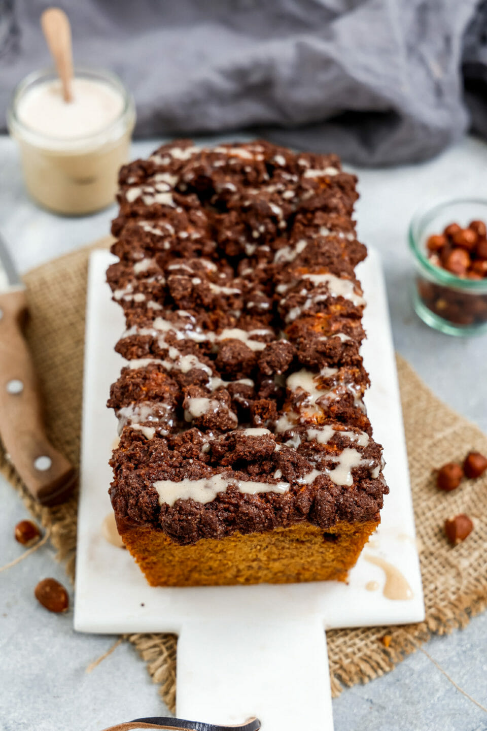 Ein Veganes Schoko-Nuss-Strudel Bananenbrot angerichtet auf einem weißen Marmorbrett dekoriert mit Haselnüssen