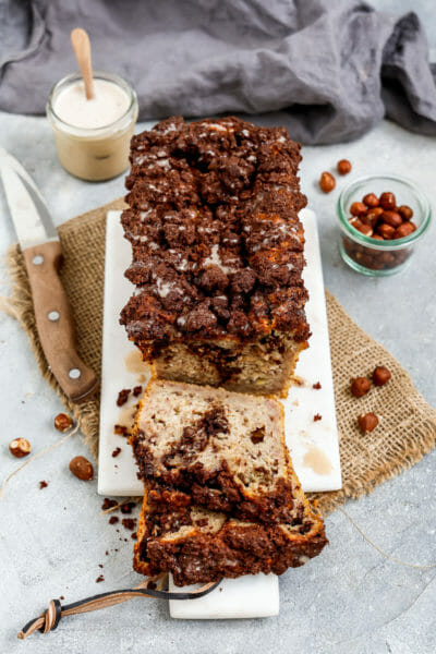 Ein Veganes Schoko-Nuss-Strudel Bananenbrot angerichtet auf einem weißen Marmorbrett dekoriert mit Haselnüssen