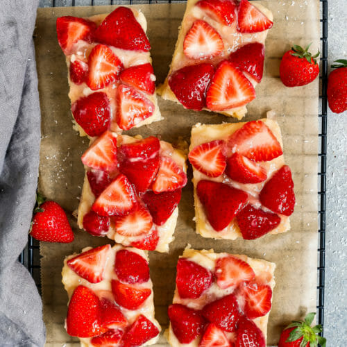 Erdbeerkuchen mit Vanillepudding, angeschnitten und auf einem Backgitter platziert und mit Erdbeeren dekoriert