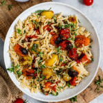 Vegane Orzo Pasta mit Tomaten serviert in einem tiefen Teller auf einem Holzbrett