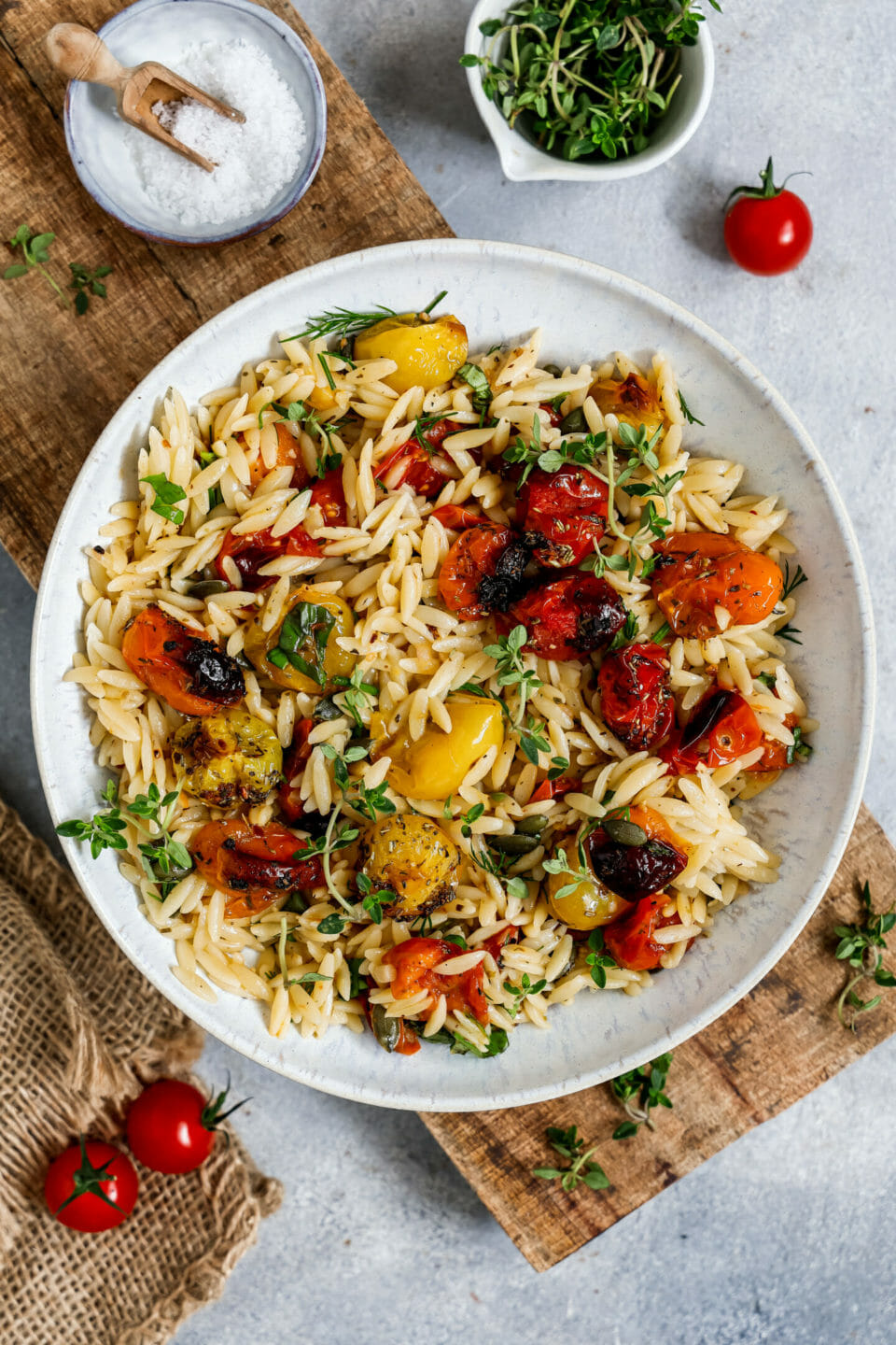 Vegane Orzo Pasta mit Tomaten serviert in einem tiefen Teller auf einem Holzbrett