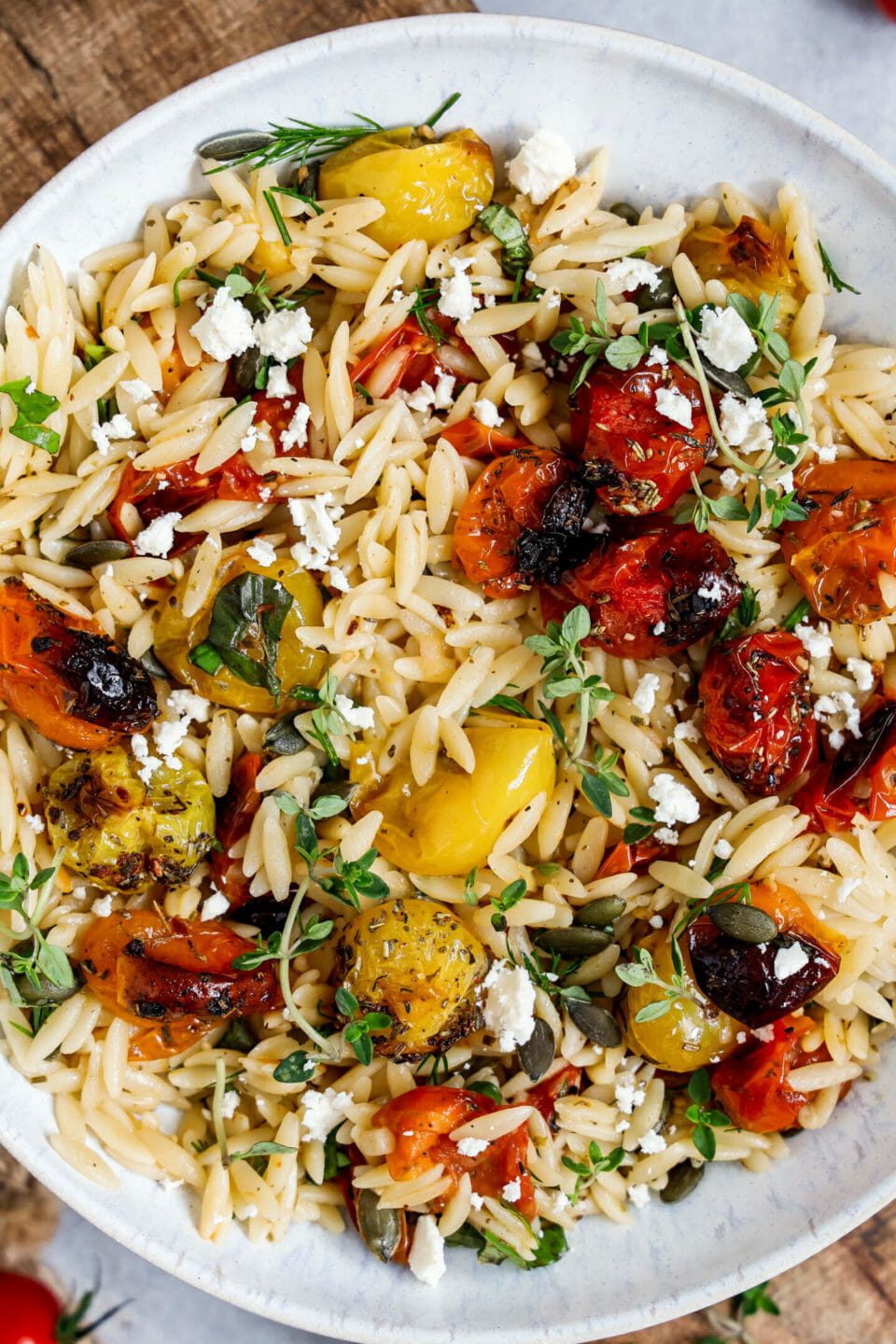 Vegane Orzo Pasta mit Tomaten serviert in einem tiefen Teller auf einem Holzbrett