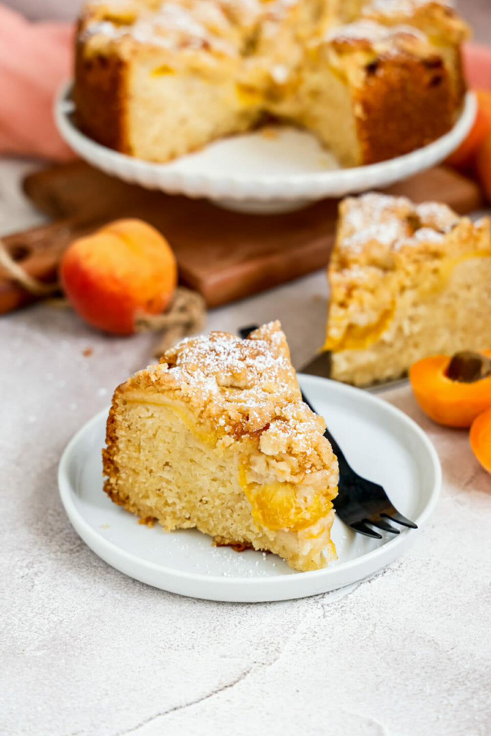 Veganer Pfirsich Streuselkuchen mit einer Kugel Eis angerichtet auf hellem Untergrund