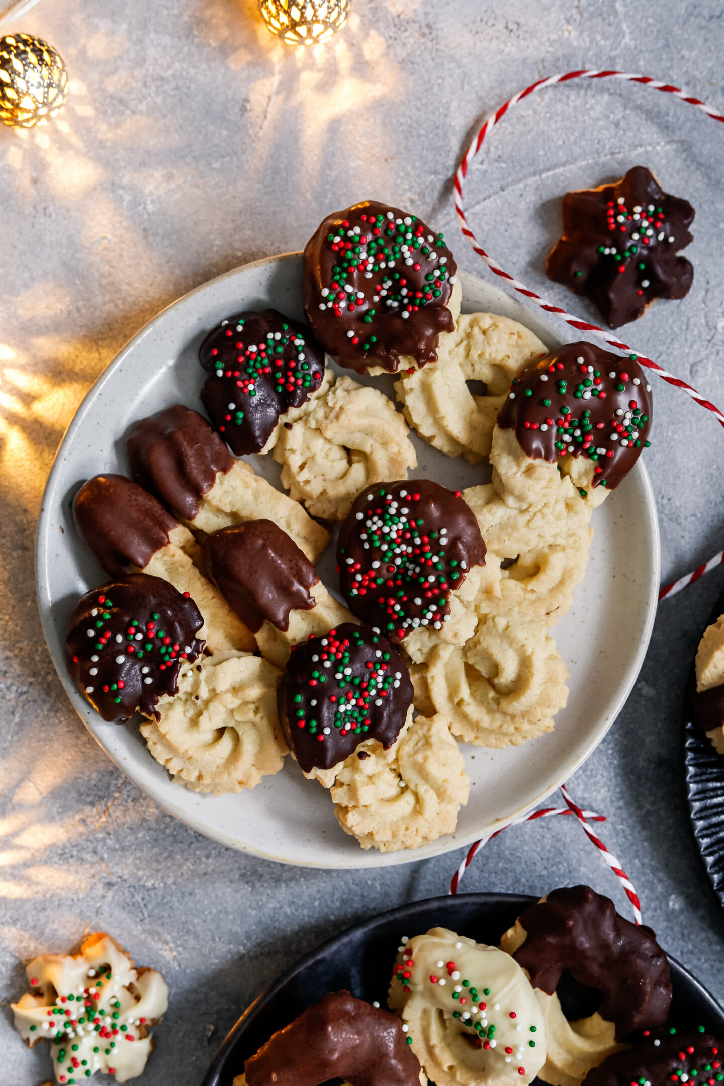 Weihnachtliches Spritzgebäck mit Mandeln und Schokolade, dekoriert mit bunten Perlen und angerichtet auf einem dunklen Teller