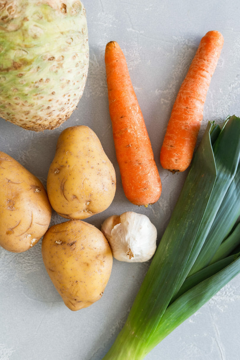 Alle Zutaten für die vegane Kartoffel-Lauch-Suppe - darunter Lauch, Kartoffeln, Möhren, Knoblauch und Knollensellerie.
