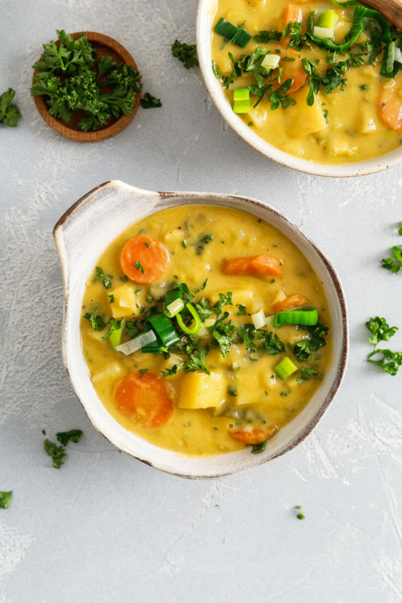 Einfaches Rezept für vegane Kartoffel-Lauch-Suppe. Der Kartoffeleintopf wird in einer Schale auf hellem Hintergrund und mit Petersilie garniert serviert.