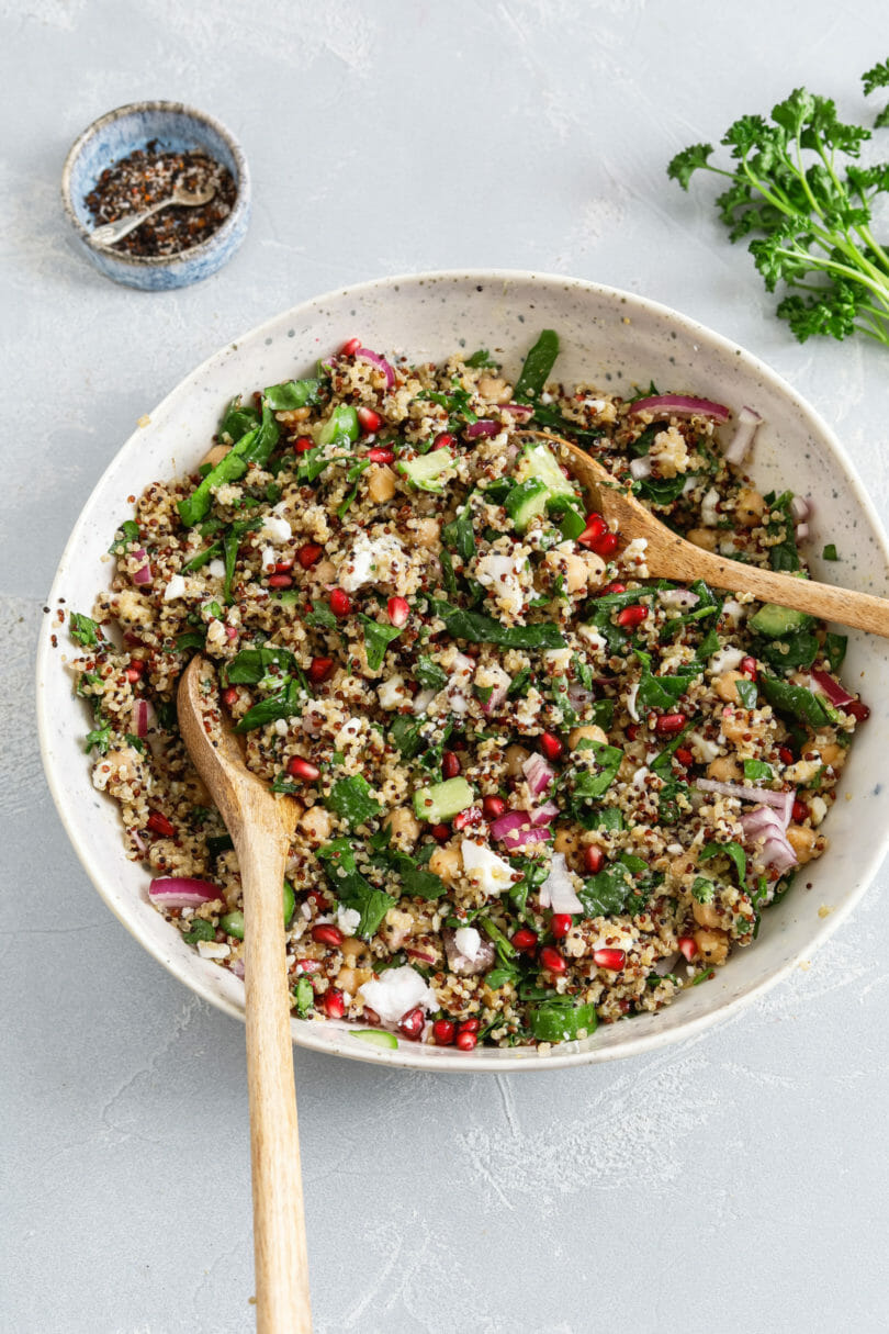 Ein leckerer Salat mit Quinoa in einem tiefen Teller auf grauem Untergrund. Der vegane Quinoa Salat wird mit Granatapfel und Kichererbsen serviert.