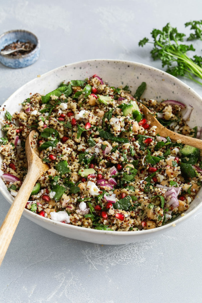 Frischer veganer Quinoa Salat mit zartem Babyspinat, fruchtigen Granatapfelkernen, Zwiebeln, veganem Feta und Kichererbsen in einer tiefen Schüssel serviert