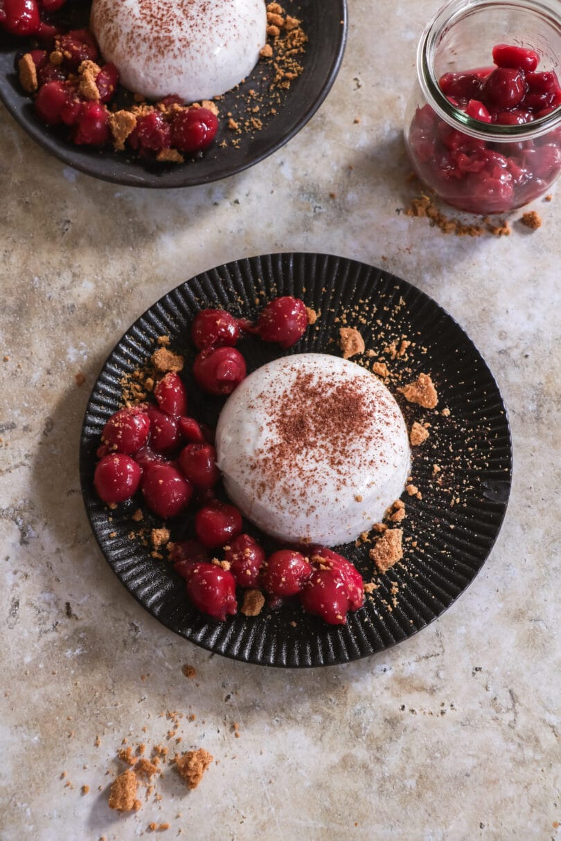 Vegane Panna Cotta ohne Gelantine mit Agar Agar zum selber machen auf einem schwarzen Teller mit Kirschen angerichtet