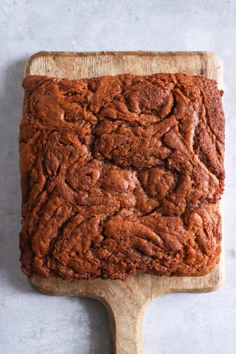 Veganer Zimtschneckenkuchen - noch ungeschnitten - auf einem Holzbrett