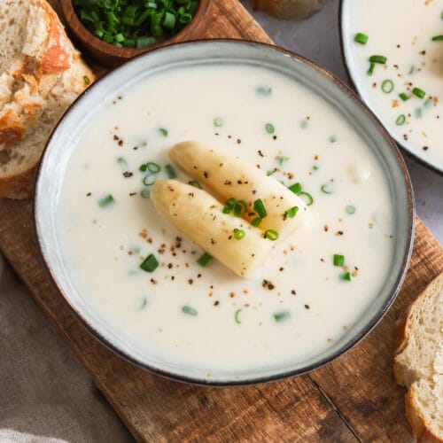 Zwei Suppenschüsseln mit veganer Spargelcremesuppe & Brot auf einem Schneidebrett