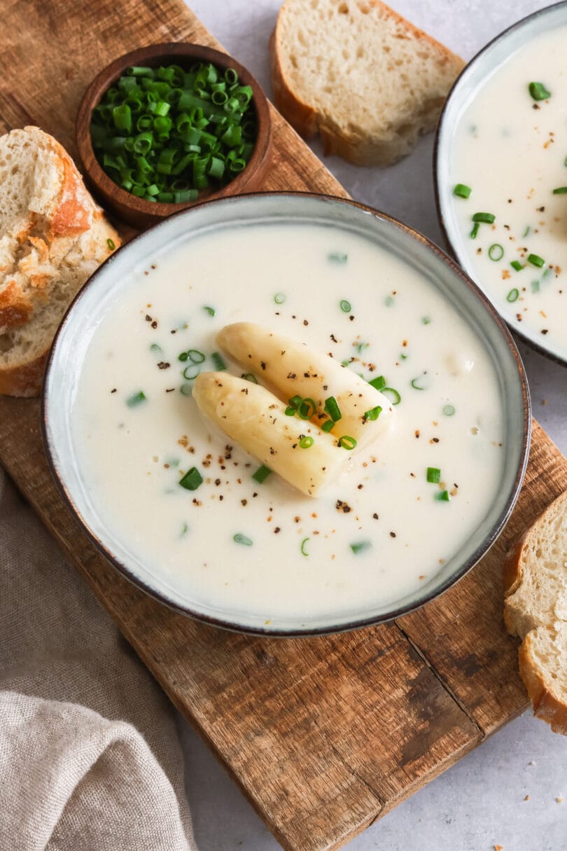 Zwei Suppenschüsseln mit veganer Spargelcremesuppe & Brot auf einem Schneidebrett