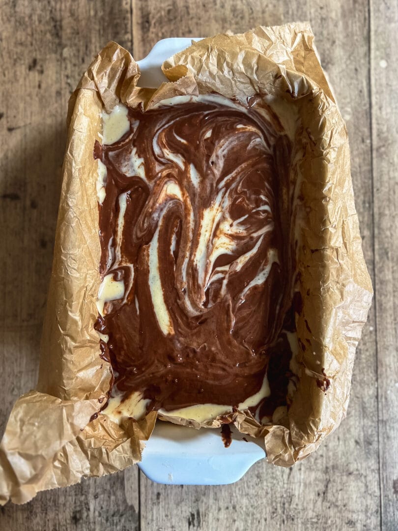 Ein Stück veganer Donauwellen-Kuchen, bestehend aus hellem und dunklem Teig mit Kirschen und Schokoladenglasur.