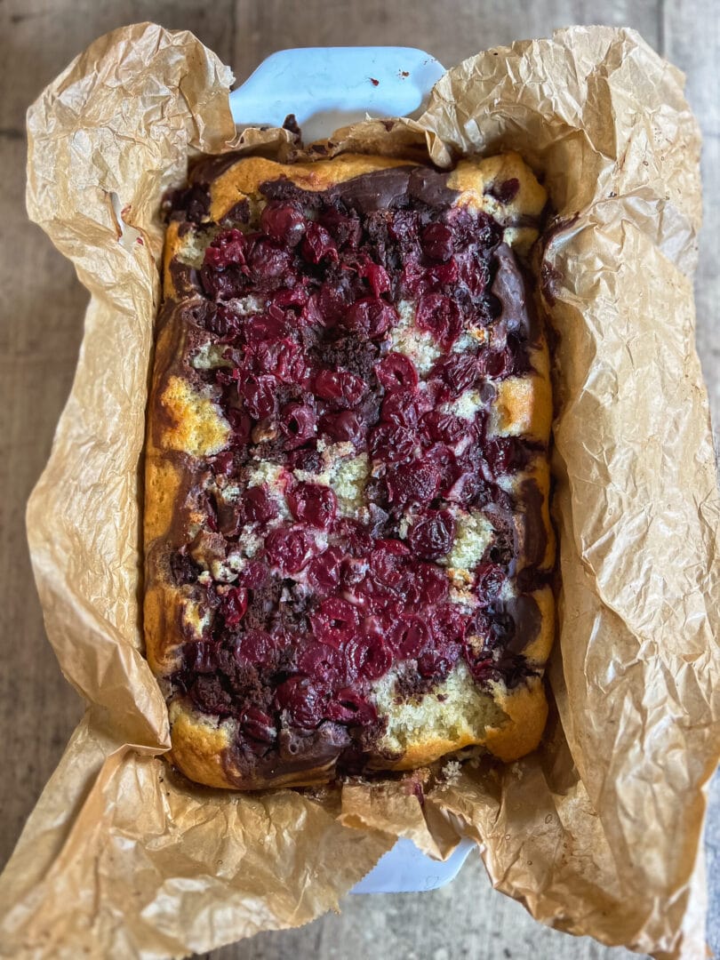 Ein Stück veganer Donauwellen-Kuchen, bestehend aus hellem und dunklem Teig mit Kirschen und Schokoladenglasur.