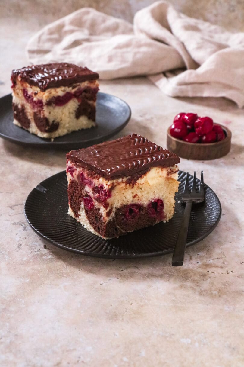 Ein Stück veganer Donauwellen-Kuchen, bestehend aus hellem und dunklem Teig mit Kirschen und Schokoladenglasur.