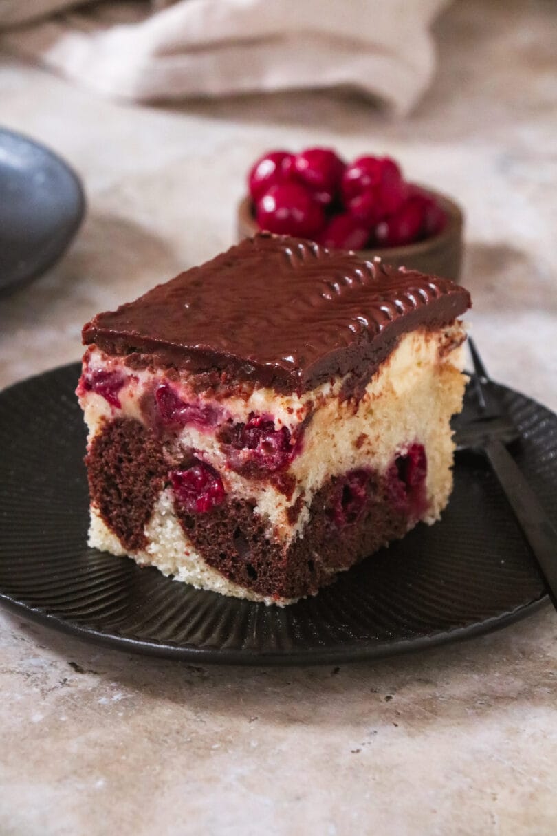 Ein Stück veganer Donauwellen-Kuchen, bestehend aus hellem und dunklem Teig mit Kirschen und Schokoladenglasur.