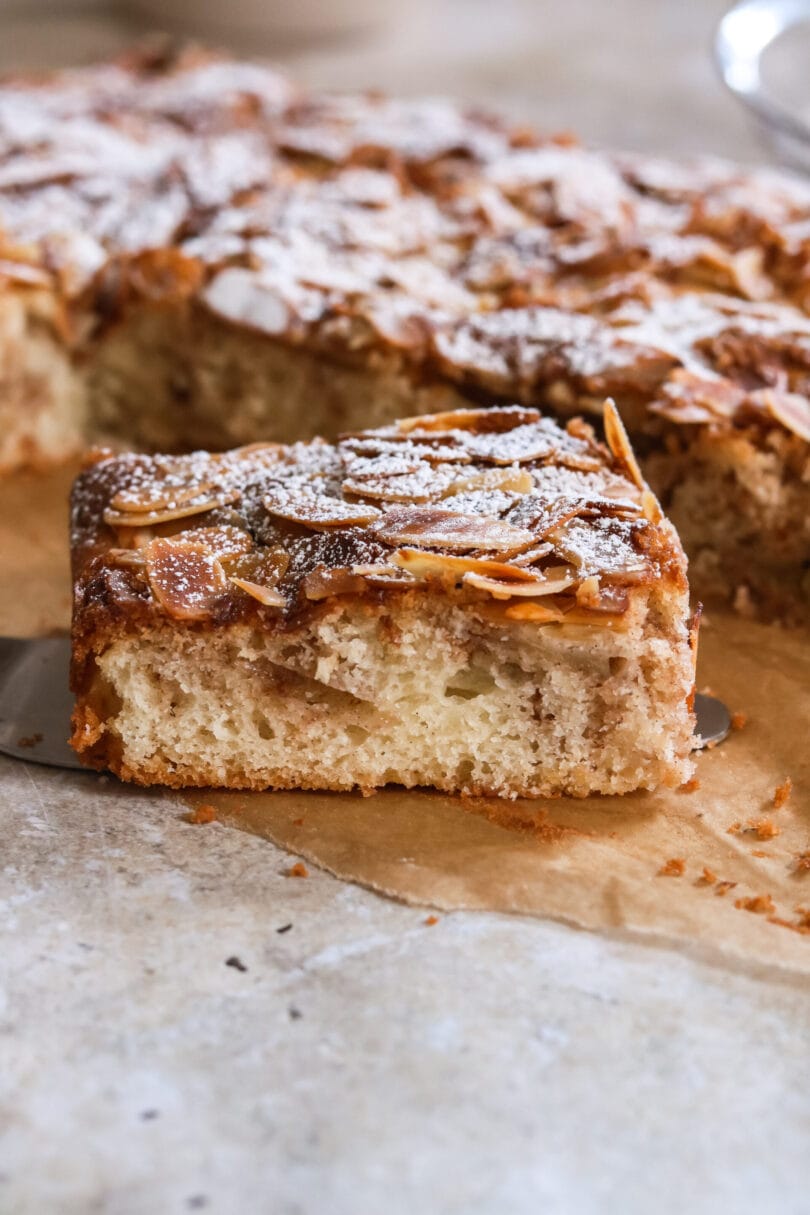 Saftiger Apfel-Zimt-Kuchen mit knusprigen Mandelblättchen und Puderzucker, auf einem Stück Backpapier. Perfekt für die Herbst- und Wintersaison.