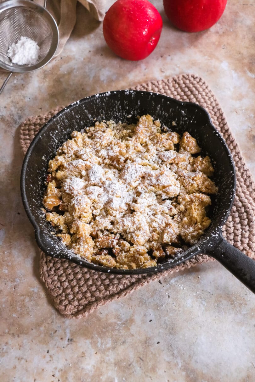 Veganer Apfelcrumble mit Puderzücker bestäubt in einer Pfanne aus Gusseisen