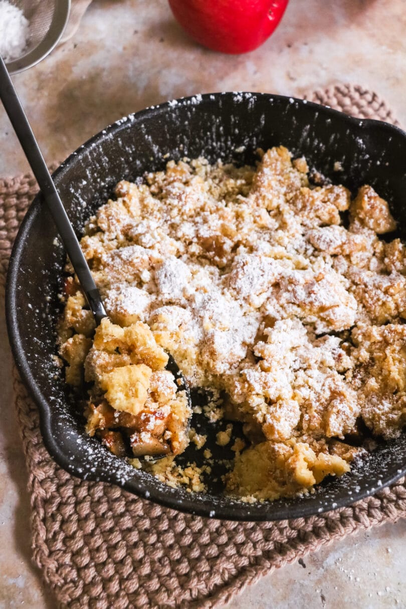 Veganer Apfelcrumble mit Puderzücker bestäubt in einer Pfanne aus Gusseisen