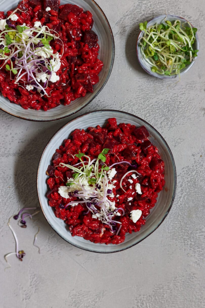 Ein Teller mit leuchtend rotem Rote-Bete-Risotto, garniert mit veganem, zerbröckeltem Feta und frischen Sprossen.
