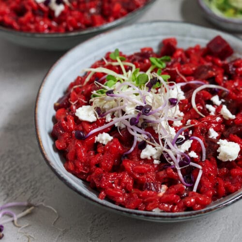 Ein Teller mit leuchtend rotem Rote-Bete-Risotto, garniert mit veganem, zerbröckeltem Feta und frischen Sprossen.