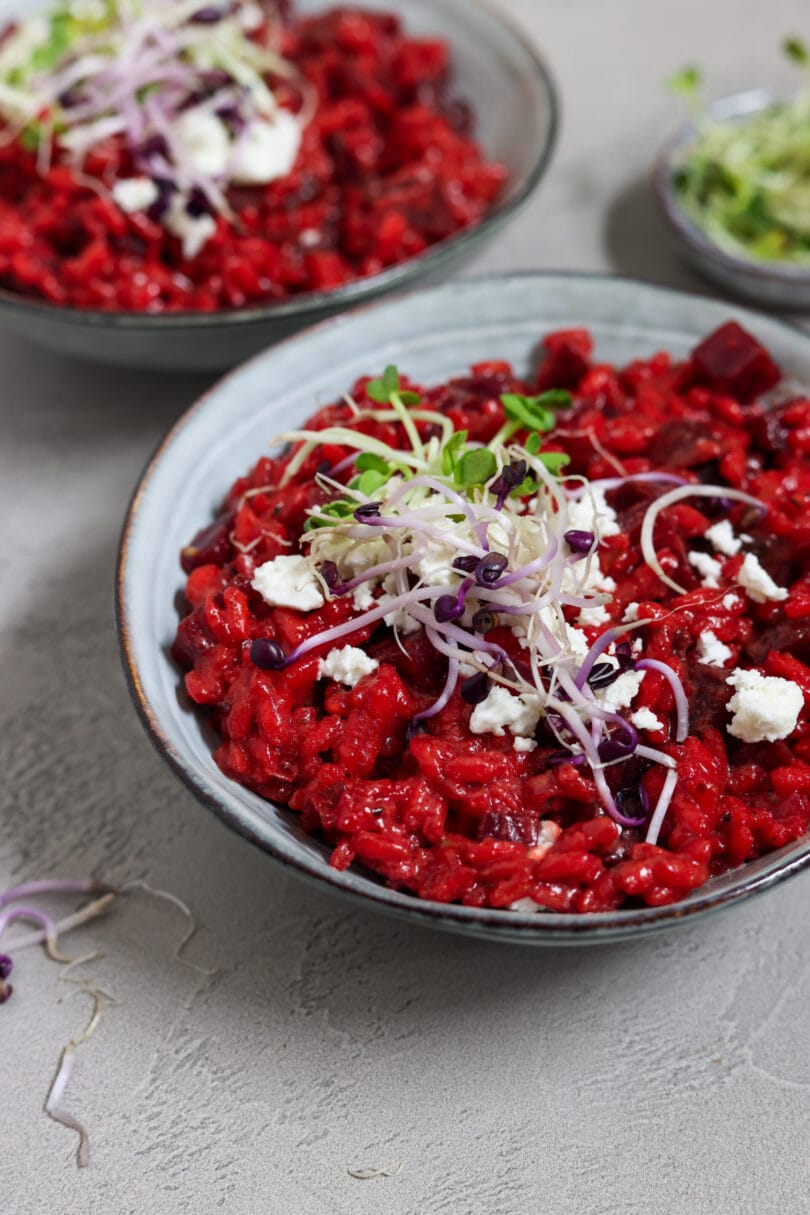 Ein Teller mit leuchtend rotem Rote-Bete-Risotto, garniert mit veganem, zerbröckeltem Feta und frischen Sprossen.