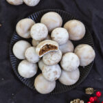 Vegane, weiße Pfeffernüsse auf einem scharzen Teller mit Weihnachtsdekoration