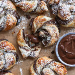 Schokoladige Nutella-Blätterteig-Schnecken auf einem Backblech, mit Puderzucker bestreut.