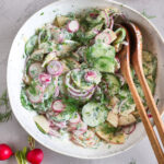 Veganer Radieschensalat mit Apfel, Gurke und cremigem Joghurtdressing in einer weißen Schüssel mit Holzlöffeln.