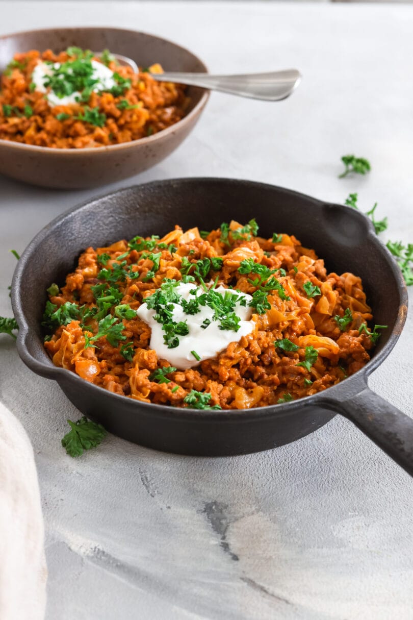Herzhafte Spitzkohlpfanne mit veganem Hack, garniert mit einem Klecks Creme Vega und frischer Petersilie.