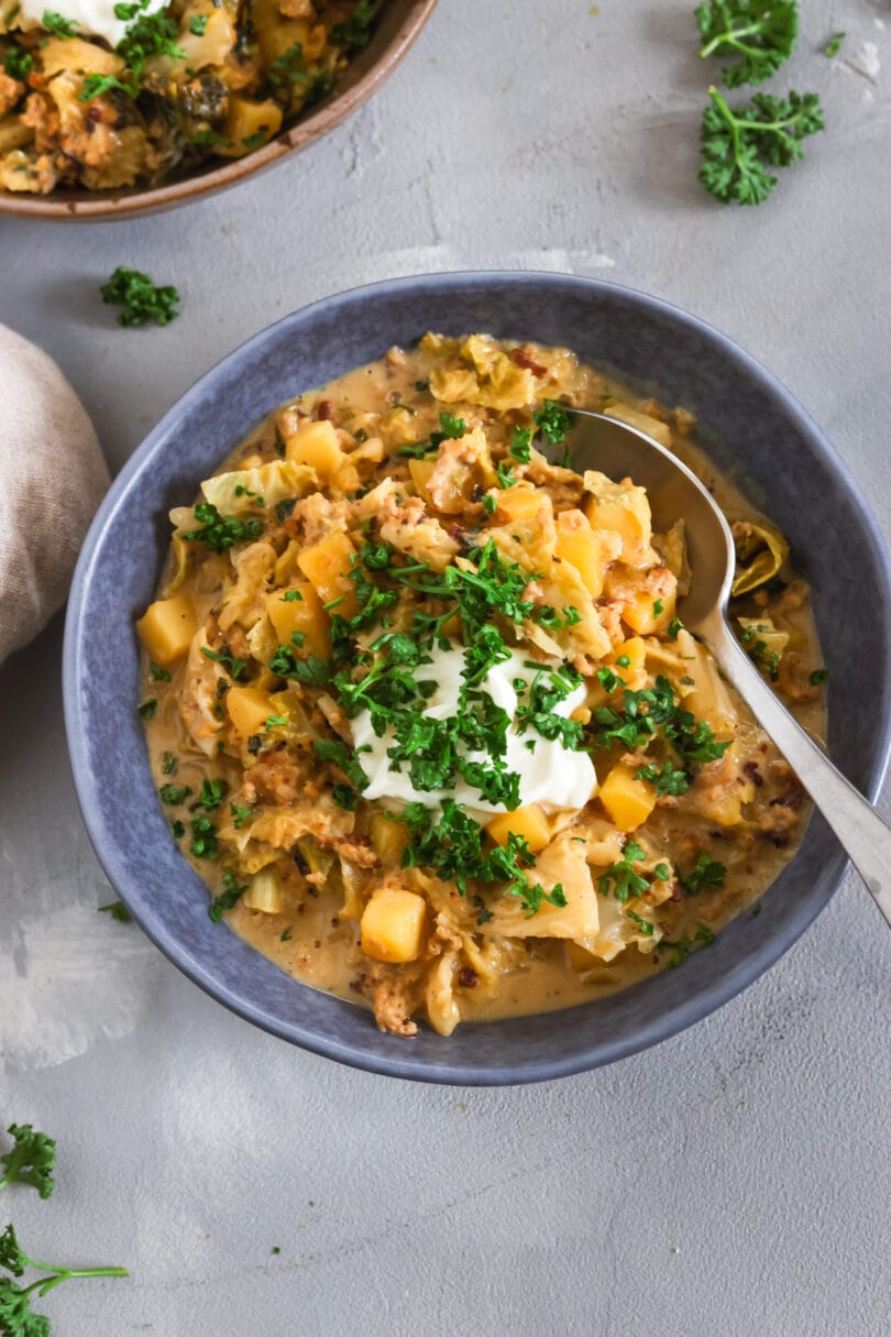 Schüssel mit cremigem Wirsingeintopf mit Kartoffelwürfeln und veganem Hack, garniert mit einem Klecks veganen Frischkäse und frischer gehackter Petersilie.