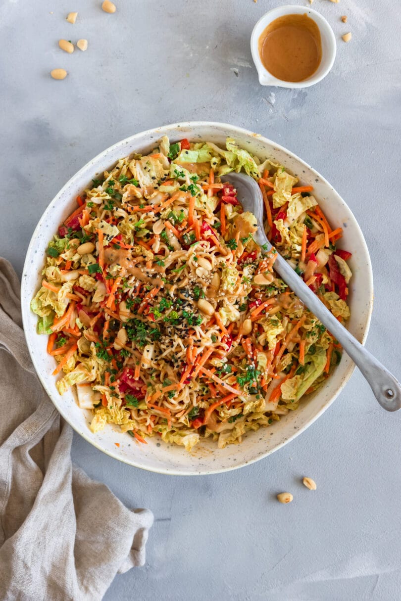 Nahaufnahme eines asiatischen Nudelsalats aus Mienudeln, Chinakohl, Karotten, Paprika und Frühlingszwiebeln mit gerösteten Erdnüssen, Sesam und cremigem Erdnuss-Kokos-Dressing.