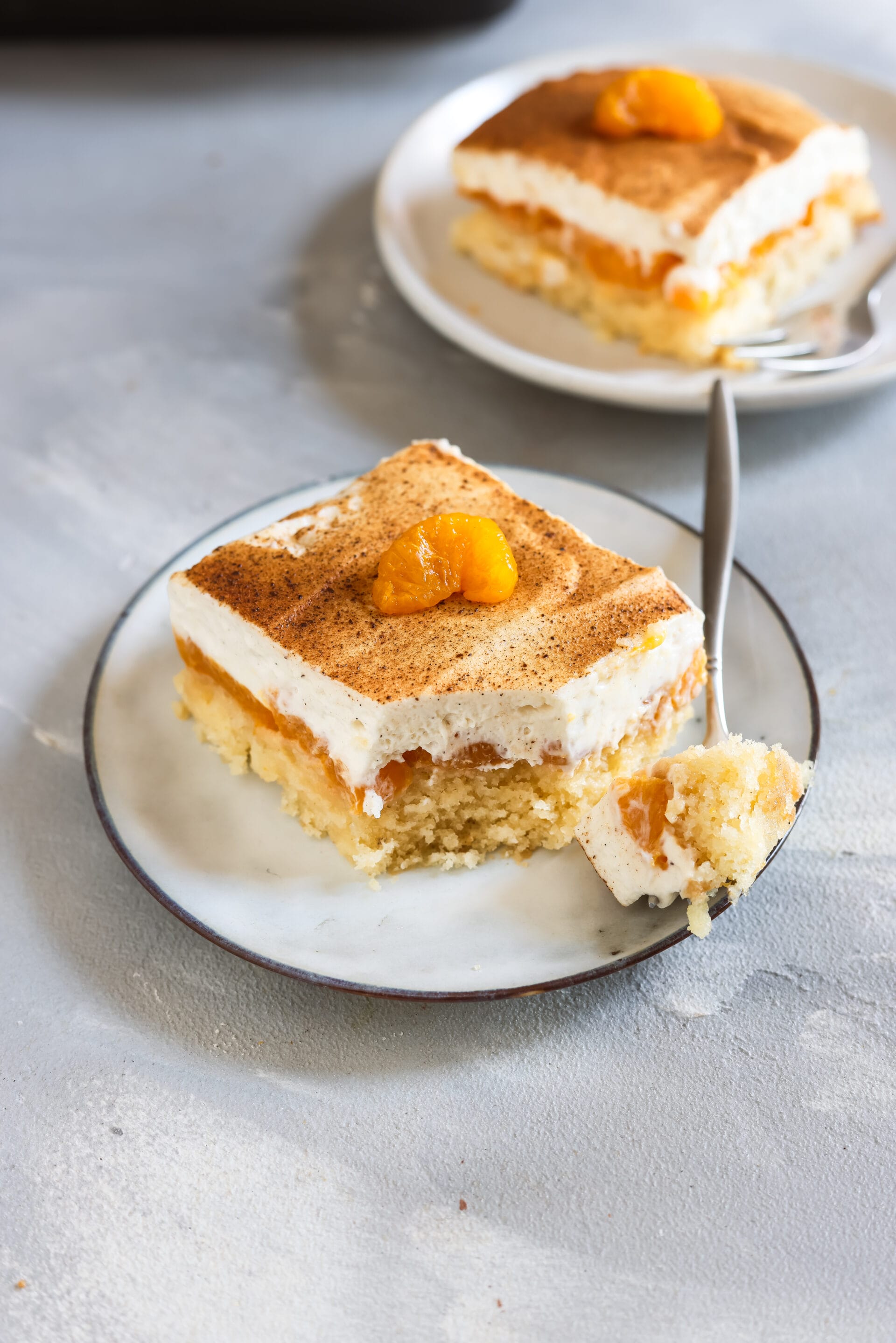 Veganer Fantakuchen mit lockerem Boden, fruchtiger Mandarinenfüllung und luftiger Creme auf einem Teller, daneben ein Löffel mit einem angeschnittenen Stück Kuchen.