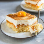 Nahaufnahme eines veganen Fantakuchens mit fluffigem Boden, Mandarinen und cremigem Topping, mit Zimt bestäubt und einer Mandarine als Dekoration.