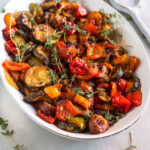 Buntes Ofengemüse mit Zucchini, Paprika, Champignons, Tomaten und Thymian in einer weißen Servierschale.