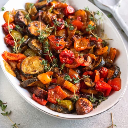 Buntes Ofengemüse mit Zucchini, Paprika, Champignons, Tomaten und Thymian in einer weißen Servierschale.