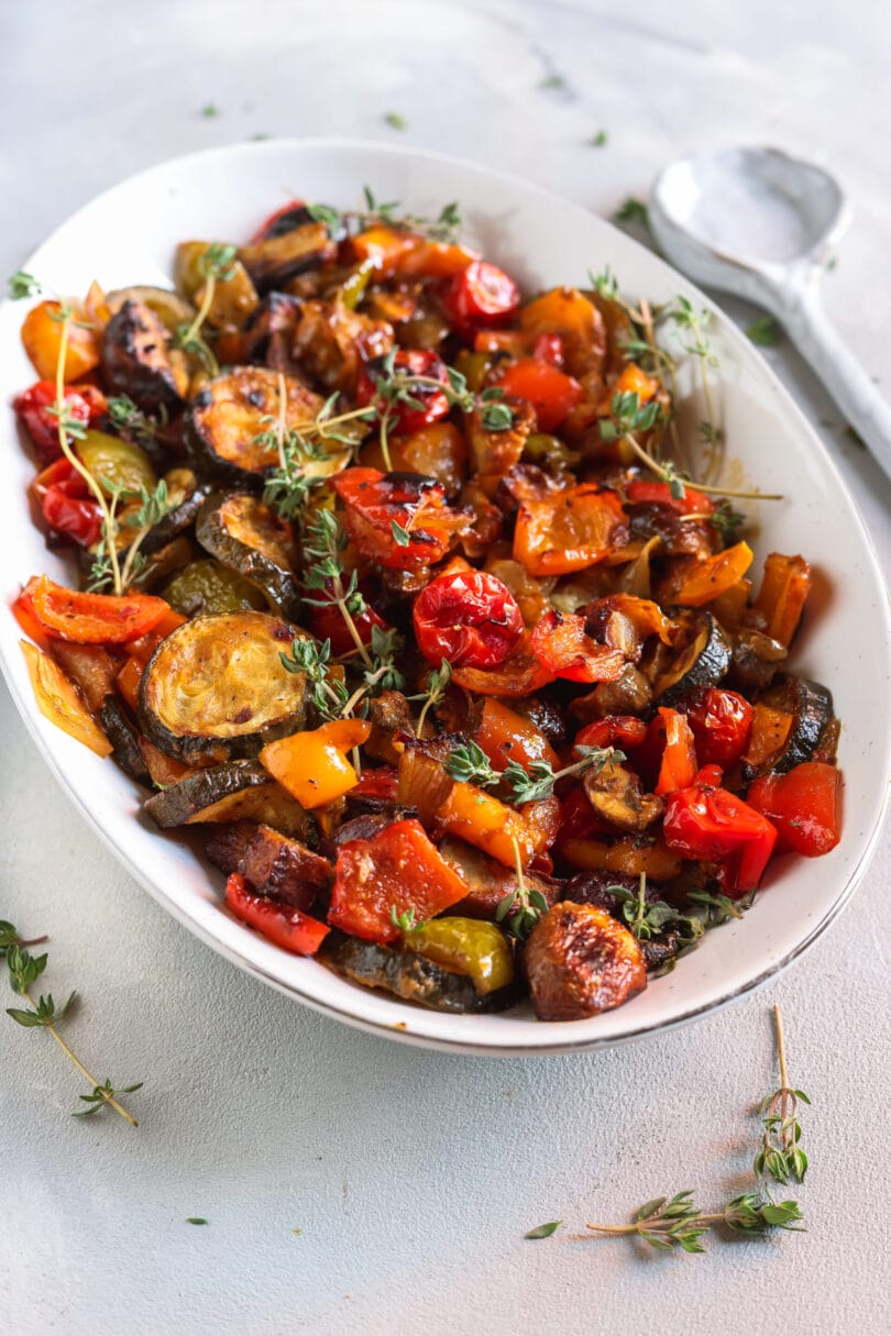 Buntes Ofengemüse mit Zucchini, Paprika, Champignons, Tomaten und Thymian in einer weißen Servierschale.