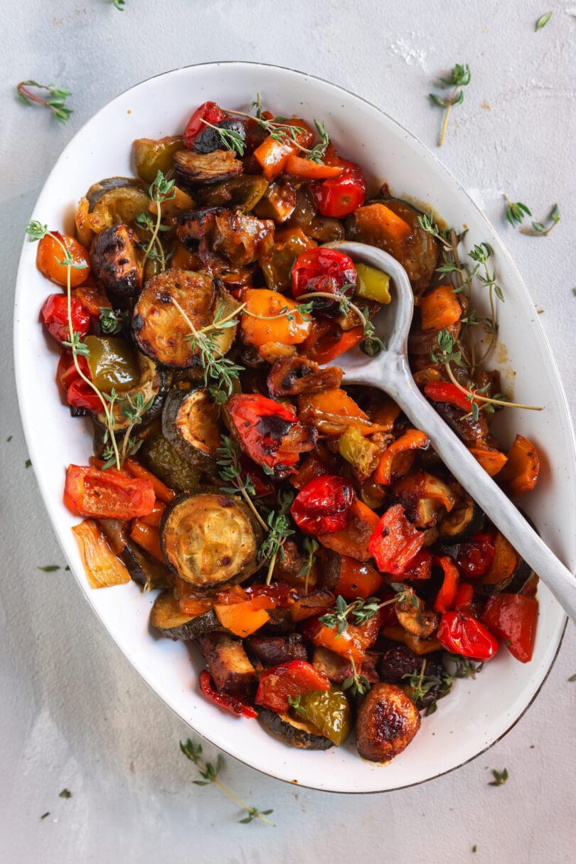 Ofengemüse mit Zucchini, Paprika, Champignons, Cherrytomaten und roten Zwiebeln, angerichtet in einer weißen Servierschale und mit frischem Thymian garniert.