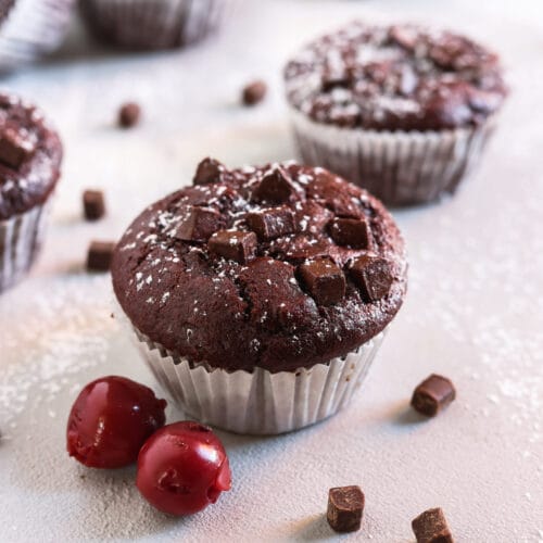 Veganer Schoko-Kirsch-Muffin mit Schokostückchen und Puderzucker, dekoriert mit frischen Kirschen.