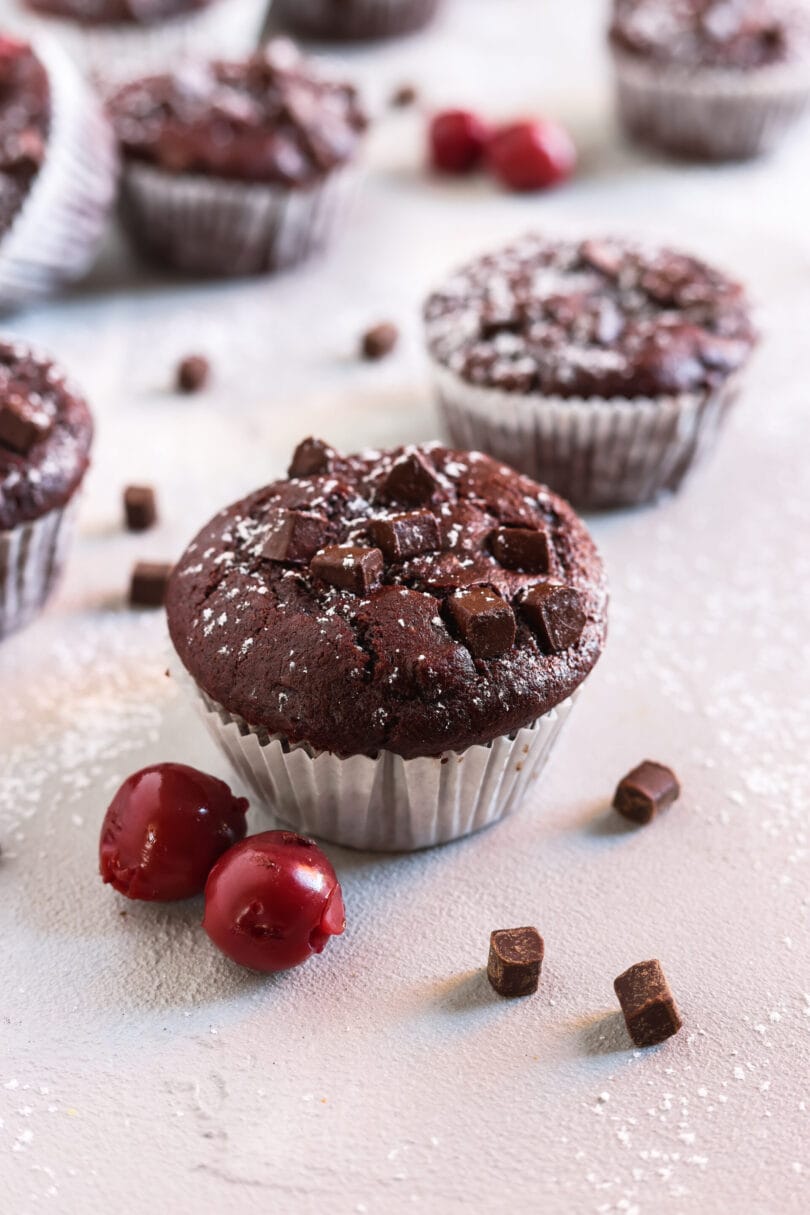 Veganer Schoko-Kirsch-Muffin mit Schokostückchen und Puderzucker, dekoriert mit frischen Kirschen.