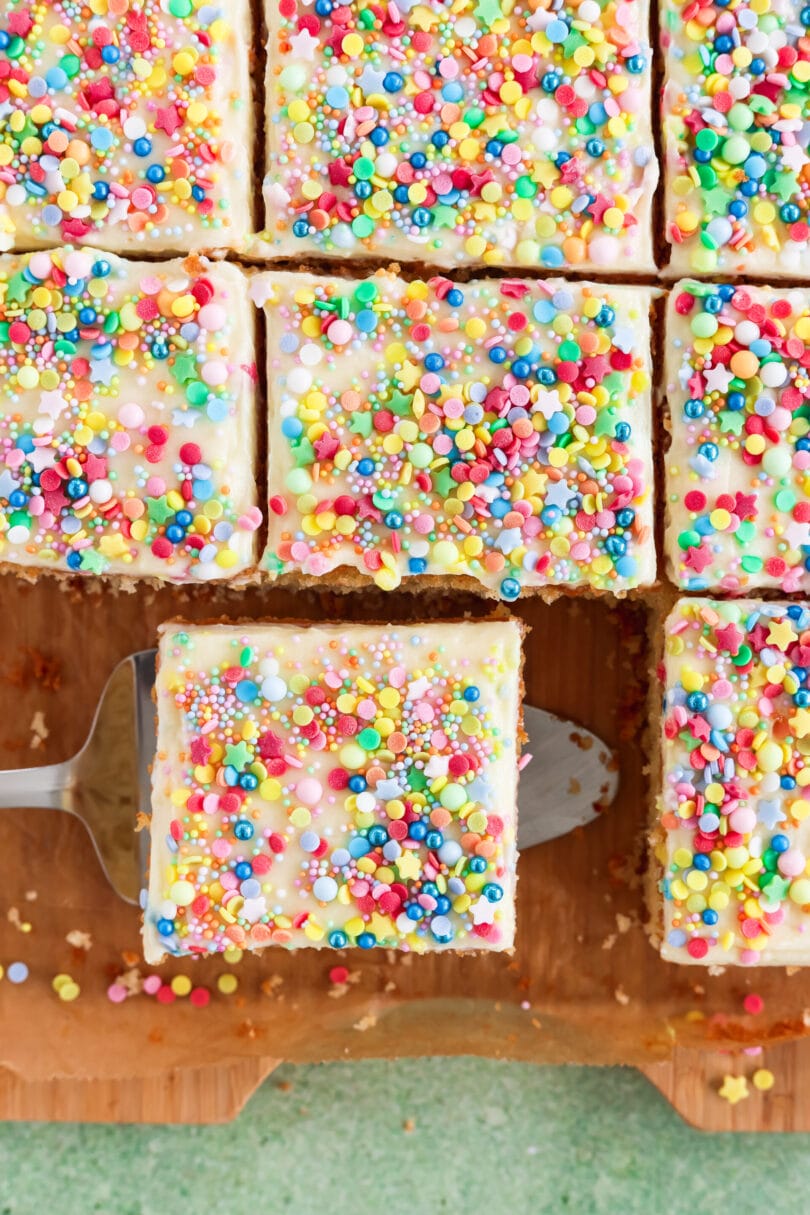 Veganer Konfettikuchen vom Blech mit cremigem Frosting und bunten Zuckerstreuseln, in quadratische Stücke geschnitten.