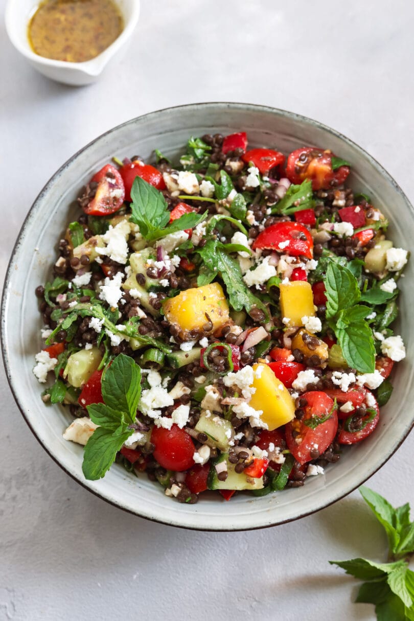 Veganer Belugalinsensalat mit Mango, Tomaten, Gurke, veganem Feta und frischer Minze in einer Schale.