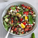 Bunter veganer Belugalinsensalat mit Mango und Feta, dazu Tomaten, Gurke, Paprika und frische Minze.