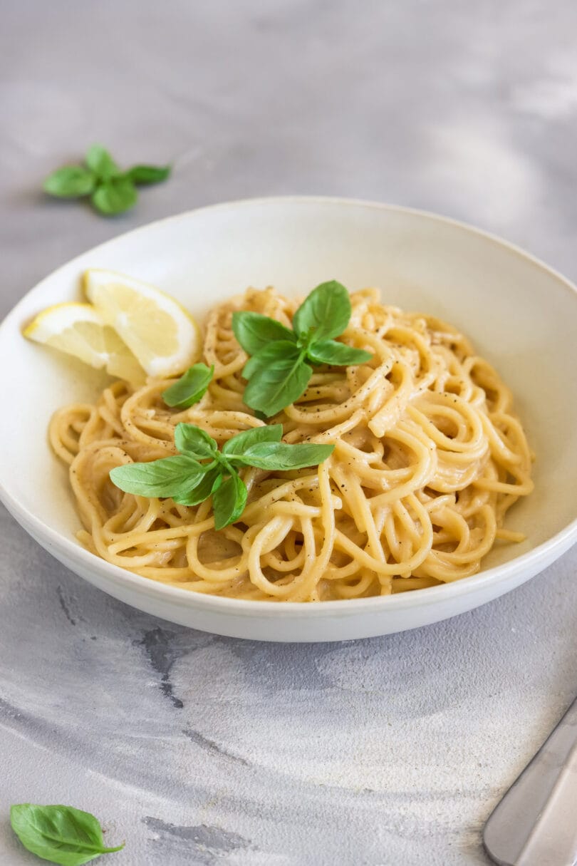 Vegane Zitronenpasta mit cremiger Sauce, frischem Basilikum und Zitronenspalten in einer hellen Schale.